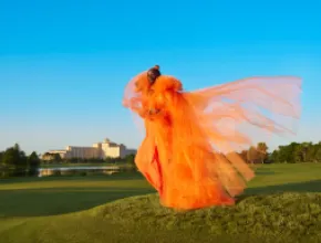 Model standing on the golf course in an orange dress in front of Rosen