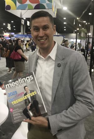 Photo of Nate Wambold at 2023 ASAE Annual Meeting & Exhibition, holding a copy of Meetings Today with his photo on the cover, in the Hub area of the exhibition floor.