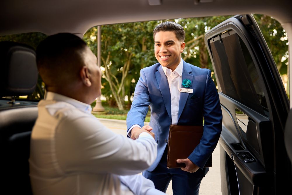 Photo of a Gaylord Hotels Celebrity Services staff member greets a guest while he is sitting in a black SUV.