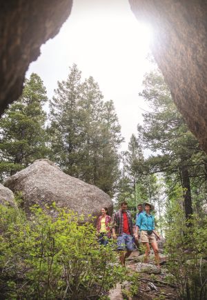 People hiking in the woods, with a big boulder in the background.