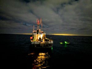 Photo of a boat in the dark sea at night, with a swimmer on the left side.