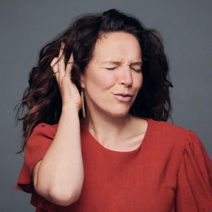 Photo of Christine Renaud in red shirt with right hand over ear.