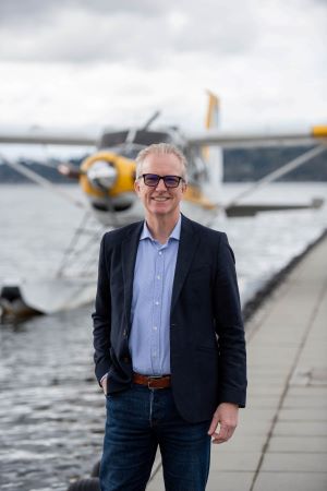 Photo of David Gudgel, standing on a dock in front of a Kenmore Air seaplane.