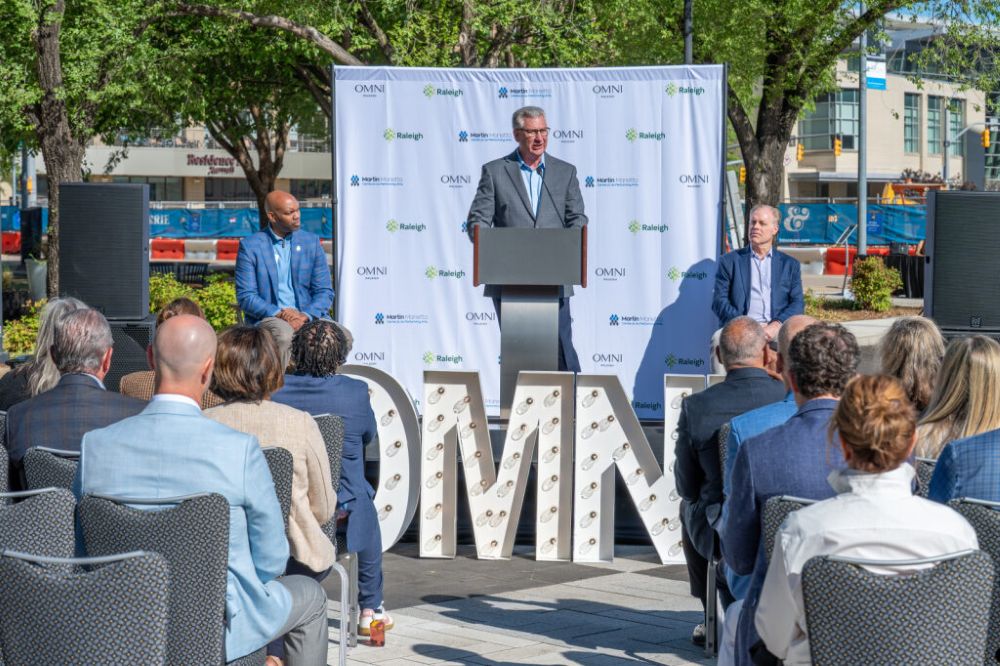 Denny Edwards speaking to a gathering of people in front of a step and repeat.