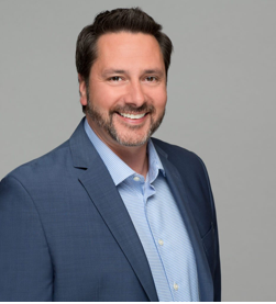 Photo of Ed Skapinok in a light blue shirt and navy blazer.