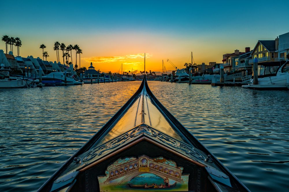 A gondola sailing through a harbor at sunset.