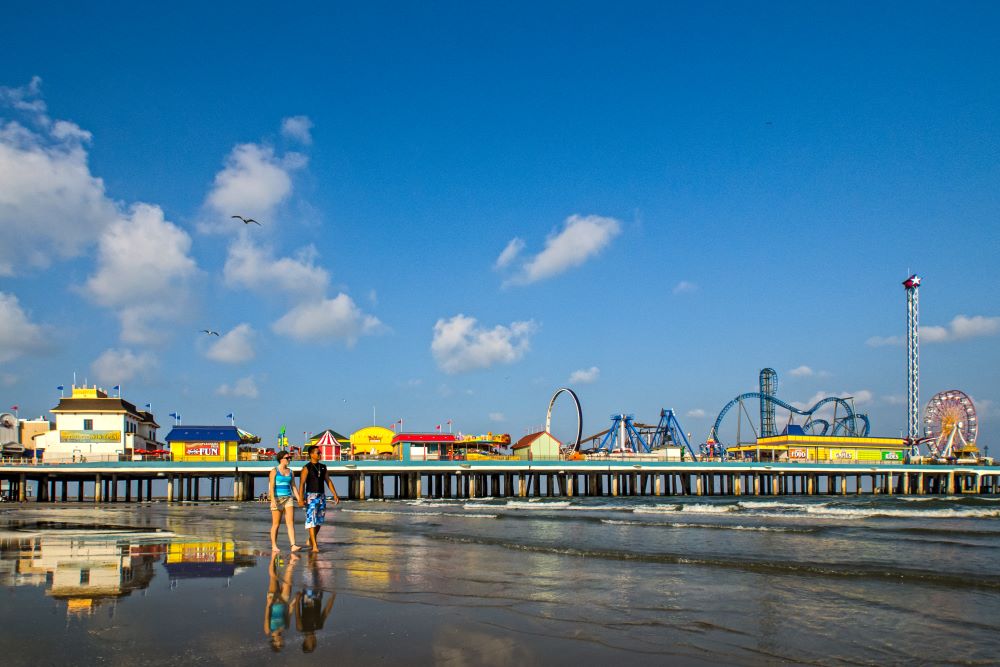 Photo of couple walking on beach in front of alveston Island Historic Pleasure Pier.