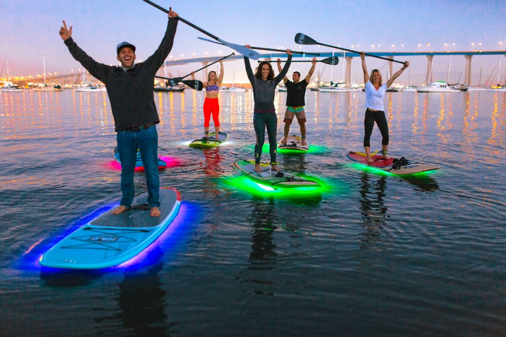Photo four people on stand-up paddleboards, raising their paddles and smiling.