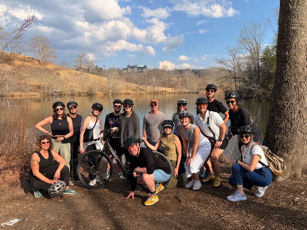 Group of people in bicycle helmets and a bike standing by a river at The Biltmore Estate.