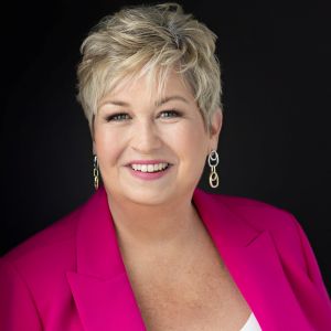 Photo of Heather Reid in a pink shirt in front of a black background.