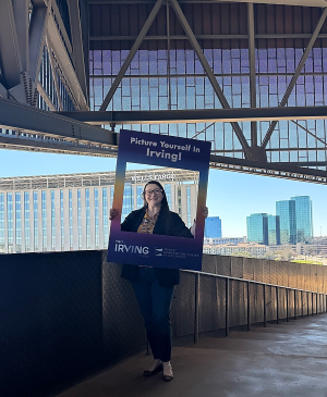 Photo of a woman holding a life-sized picture frame with the words "picture yourself in Irving" written on it.