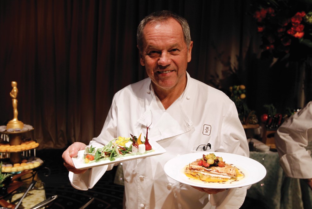 Photo of Wolfgang Puck offering plates of food.