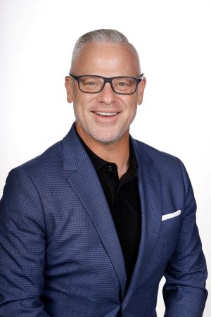 Photo of Mario J. Bass, in a blue blazer and black shirt with a white background.