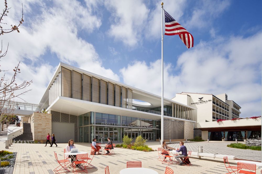 Monterey Conference Center, with an American flag in the foreground and people sitting at tables outside.
