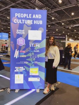 Naomi Hollas posing with signage for an event featuring Event Grads