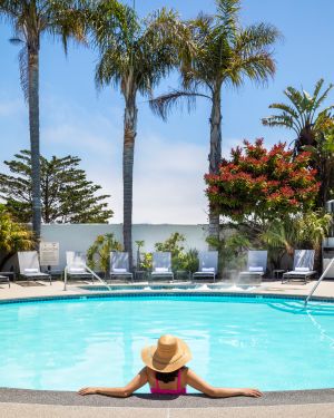 Portola Hotel & Spa pool with a woman relaxing in it, with palm trees in the background.
