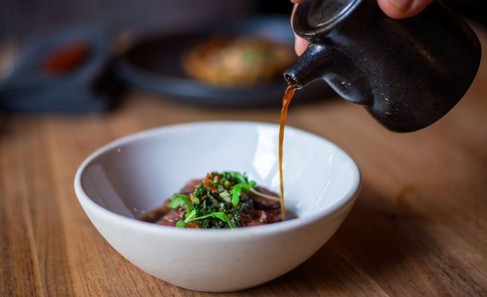 Sauce being poured on a food item in a white bowl at Légende.