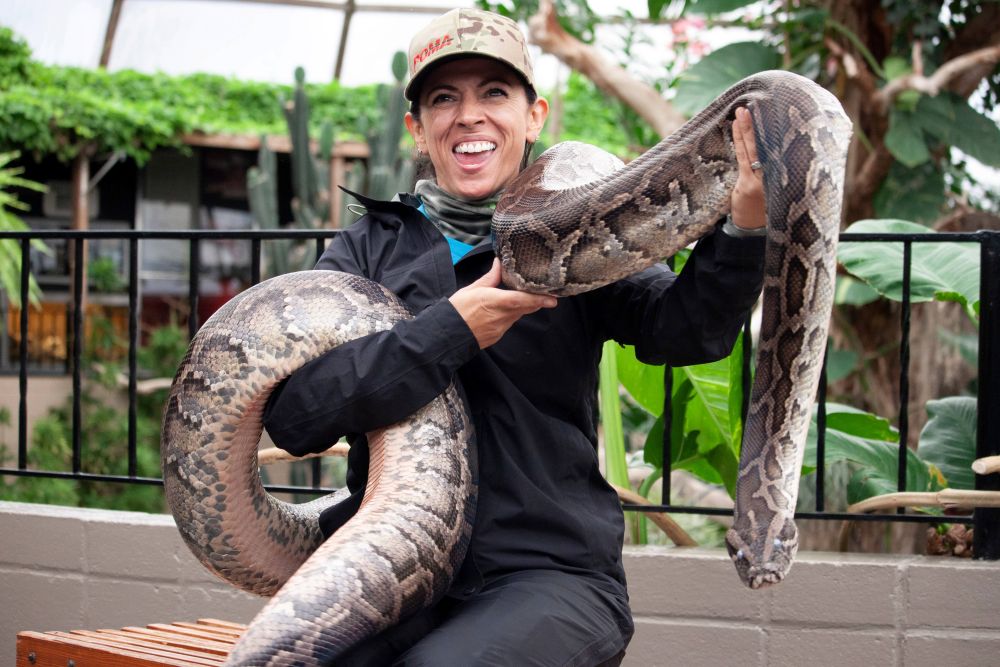 A smiling woman holding a large snake.