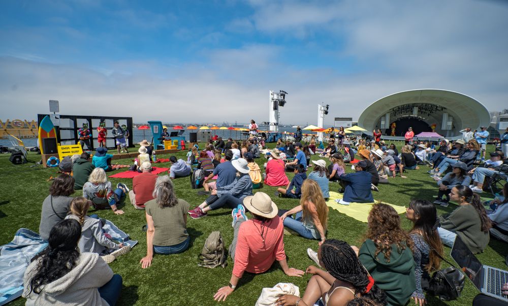 Rady Shell with people sitting on a lawn watching a performance.