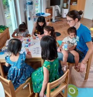 Photo of a woman sitting at a table surrounded by children.