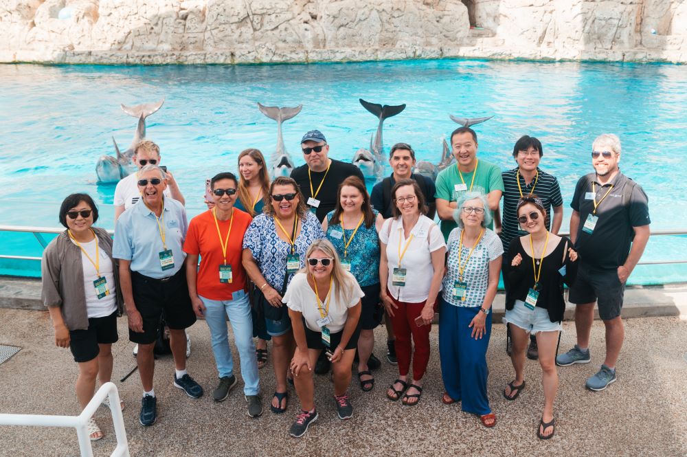 Photo of group of people posing in front of dolphins in their tank at Texas State Aquarium.