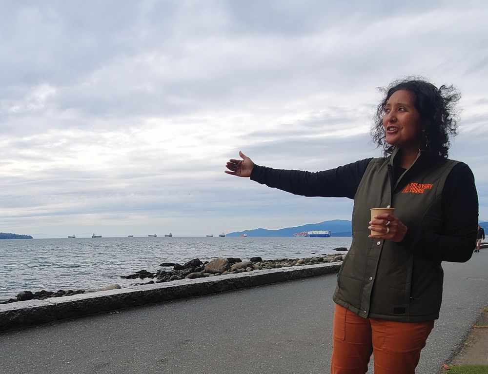 Ruby Banwait from Talaysay Tours with her arm extended looking out over the waterfront.