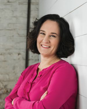 Image of Tracy Stuckrath leaning against a wall in a pink shirt.