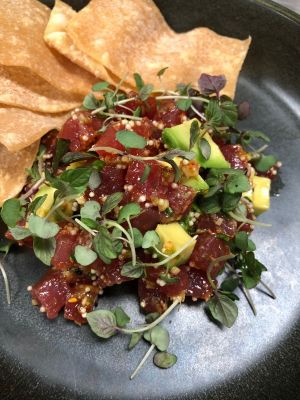 Photo of tuna tartare on a black plate with crisps.