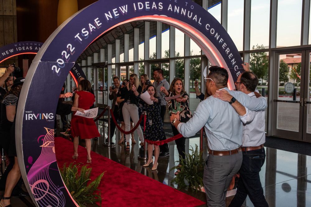 Photo of two men walking through an arch at the TSAE convention in Irving, with people cheering them on.