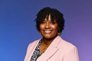 Photo of Zoe Moore, in a pink blazer in front of a blue background.