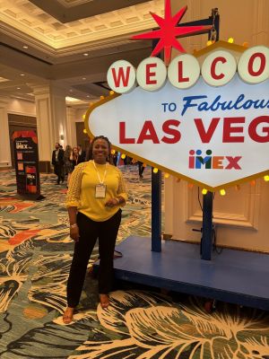 Photo of Zoe Moore standing next to a Welcome to Las Vegas sign at IMEX America.