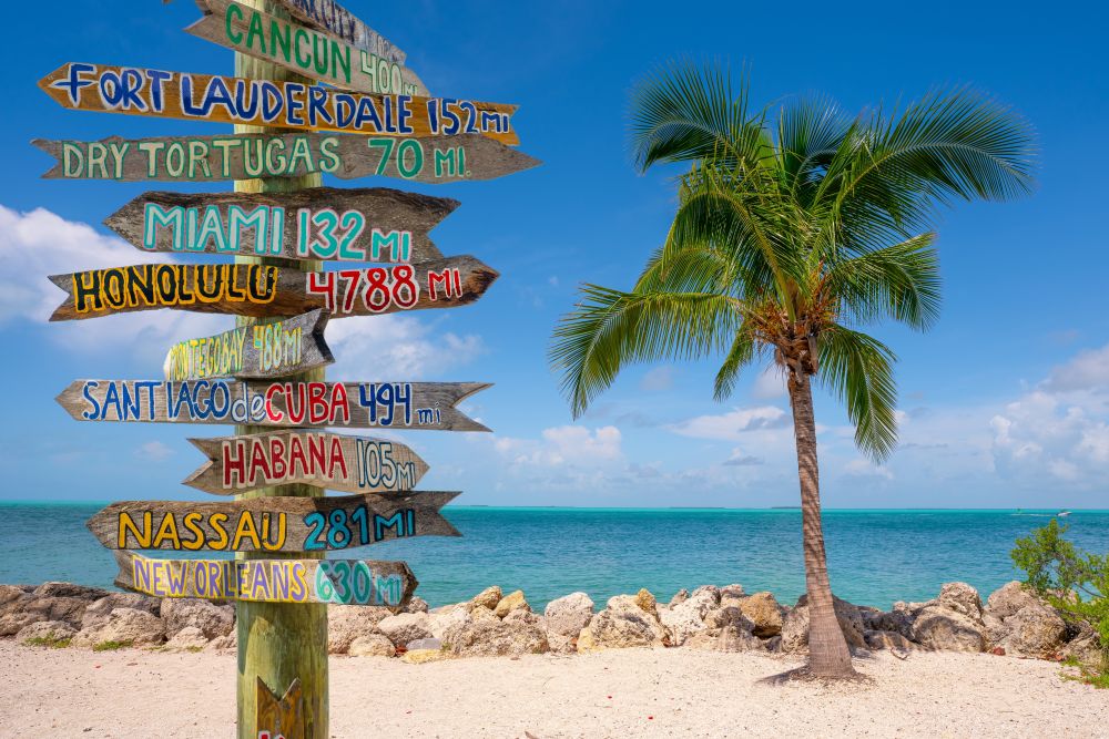 Sign in Key West on the beach with multiple destinations reflected in terms of distance from Key West.