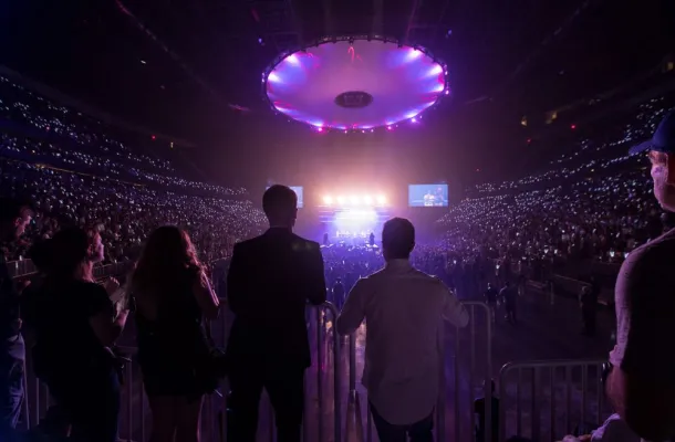 Photo of people looking at a concert, in a venue filled with purple light.