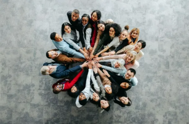 image of a bunch of people standing in a circle, with their extended hands touching in the center.