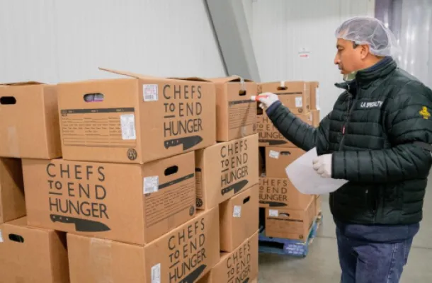 Image of a man standing in front of boxes of donated food from Chefs to End Hunger