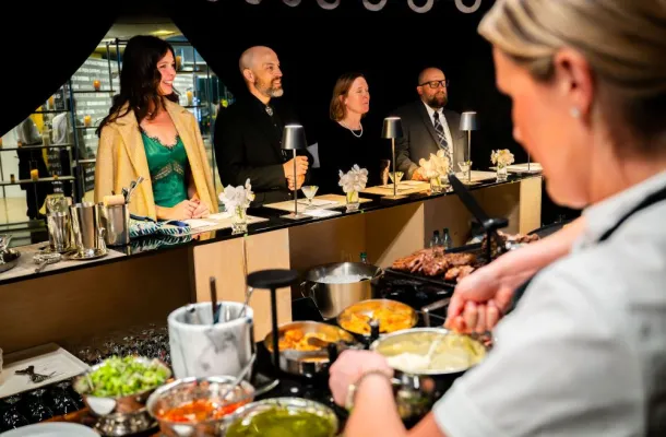 Photo of a chef preparing food in front of a small group of diners at an event.