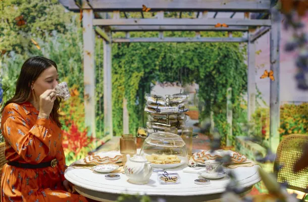 Photo of a woman in an orange dress sipping tea at a table in a garden setting.