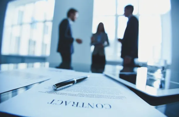 Photo of three people in the background with a contract in the forground.