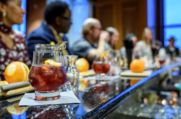 Photo of a cocktail on a bar with bar patrons behind it.