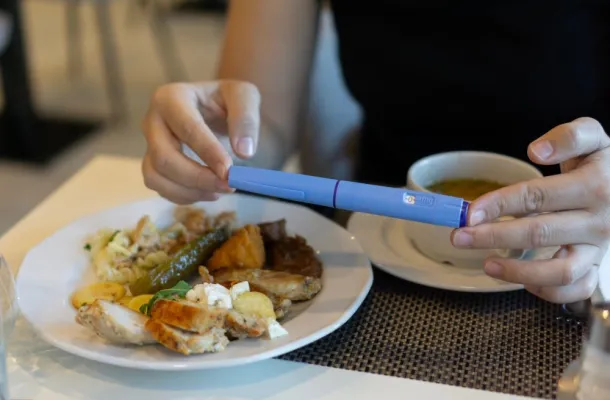 Image of a person with a GLP-1 injection pen next to a plate of food.