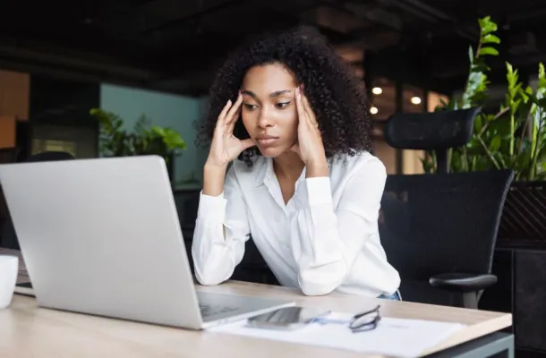 A business woman in a white blouse clasping her heads to her head in frustration, over a laptop.