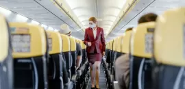 Masked flight attendant walking down airline aisle.