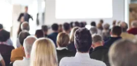 Photo of audience listening to speaker in conference center.