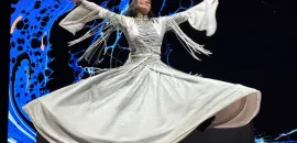 Photo of a Sufi dancer in a flowing white dress twirling on stage.