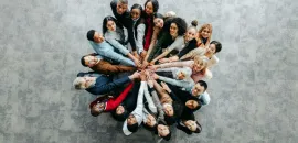 image of a bunch of people standing in a circle, with their extended hands touching in the center.