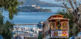 Photo of a cable car climbing a hill in San Francisco, with San Francisco Bay in the distance.