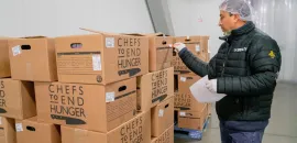 Image of a man standing in front of boxes of donated food from Chefs to End Hunger
