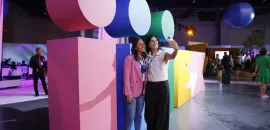 Two attendees take a selfie in front of the IMEX sign