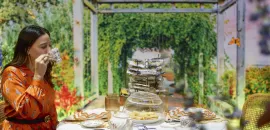 Photo of a woman in an orange dress sipping tea at a table in a garden setting.