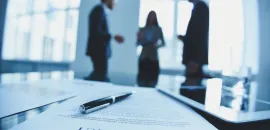 Photo of three people in the background with a contract in the forground.